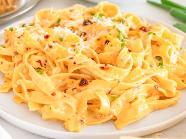 Creamy Chili Crisp Fettuccine Alfredo topped with grated cheese and fresh green herbs on a white plate.