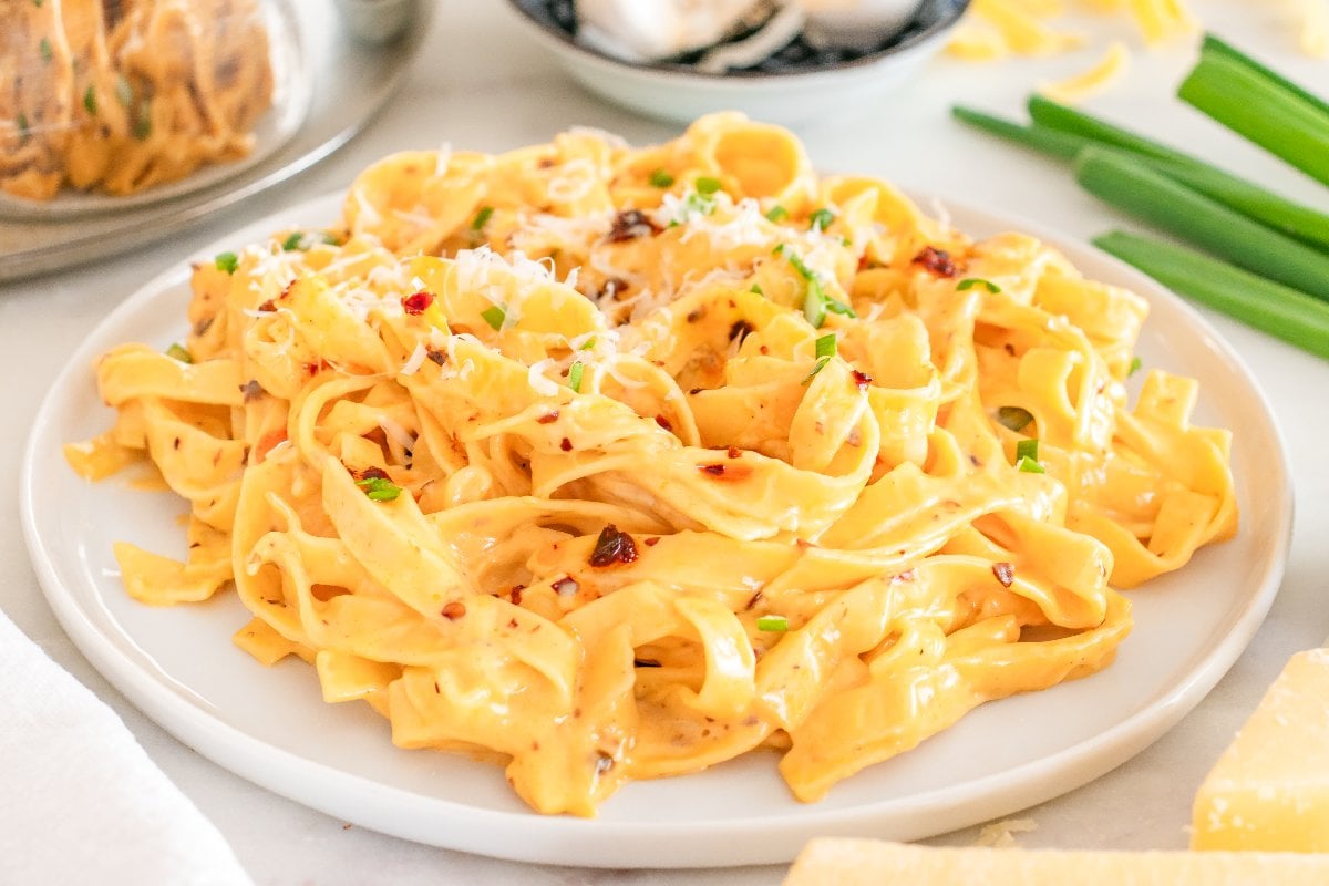 A plate of creamy Chili Crisp Fettuccine Alfredo pasta topped with grated cheese and chopped green onions.