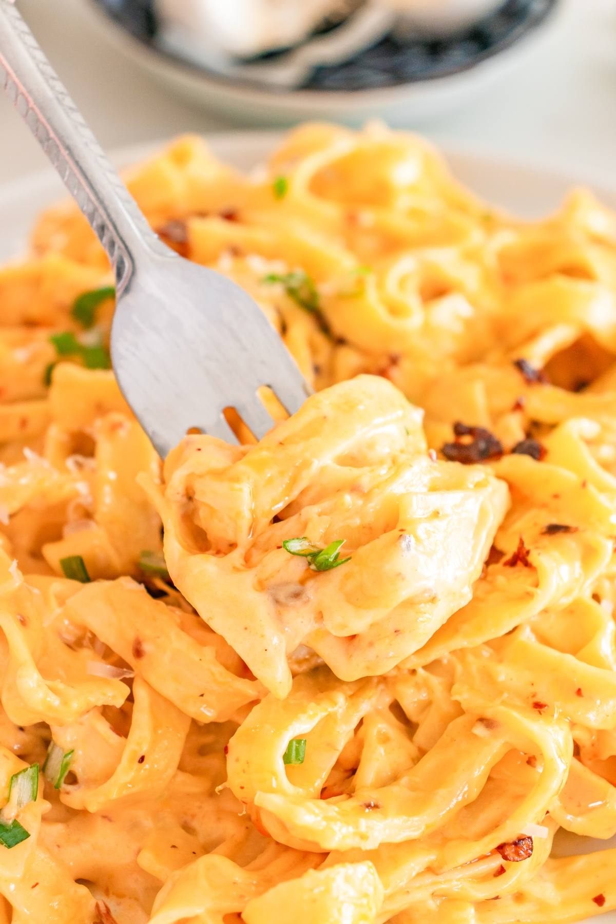 A fork twirls creamy fettuccine pasta garnished with herbs on a plate.