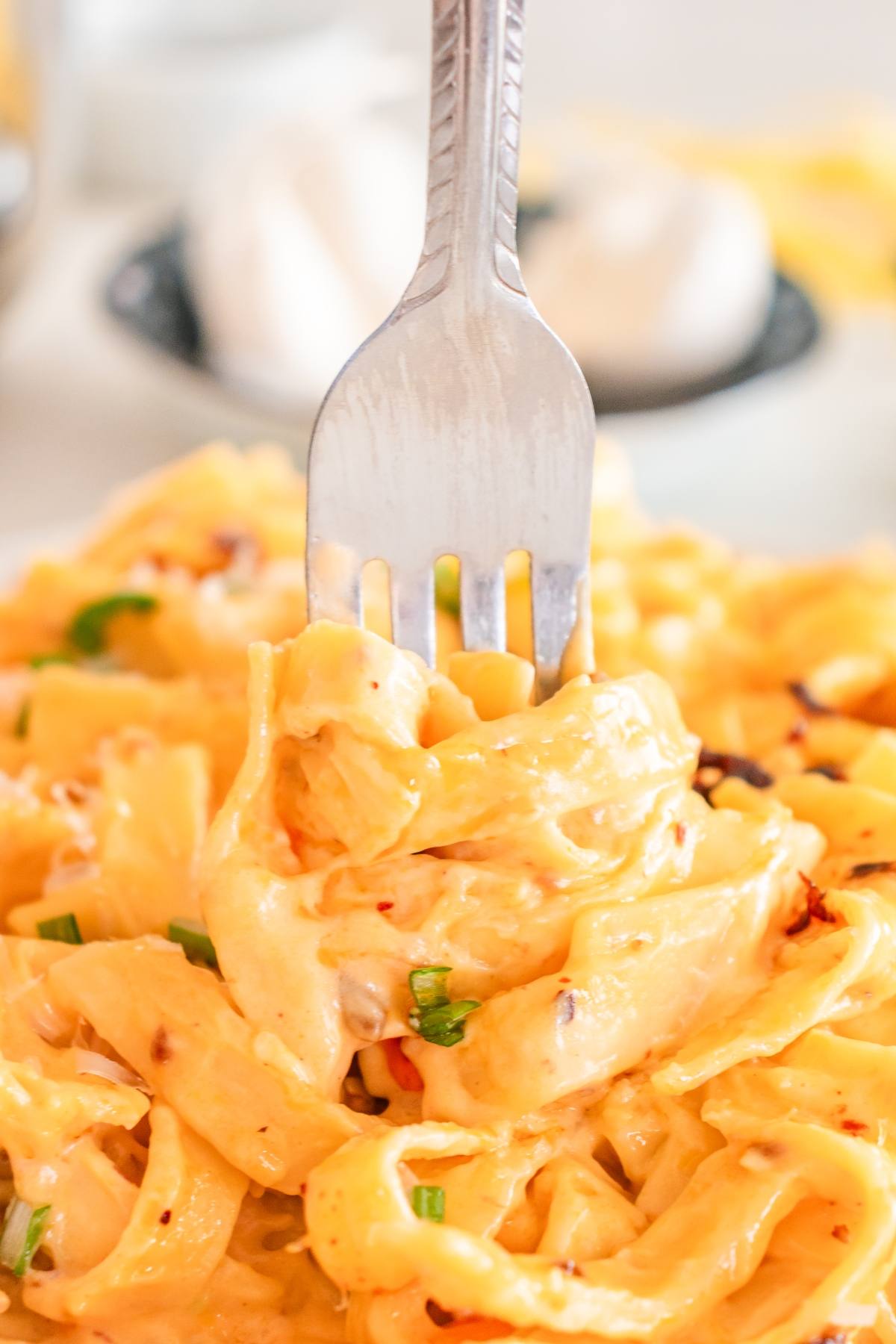 A fork twirls creamy, cheesy pasta garnished with chopped green onions and red pepper flakes.