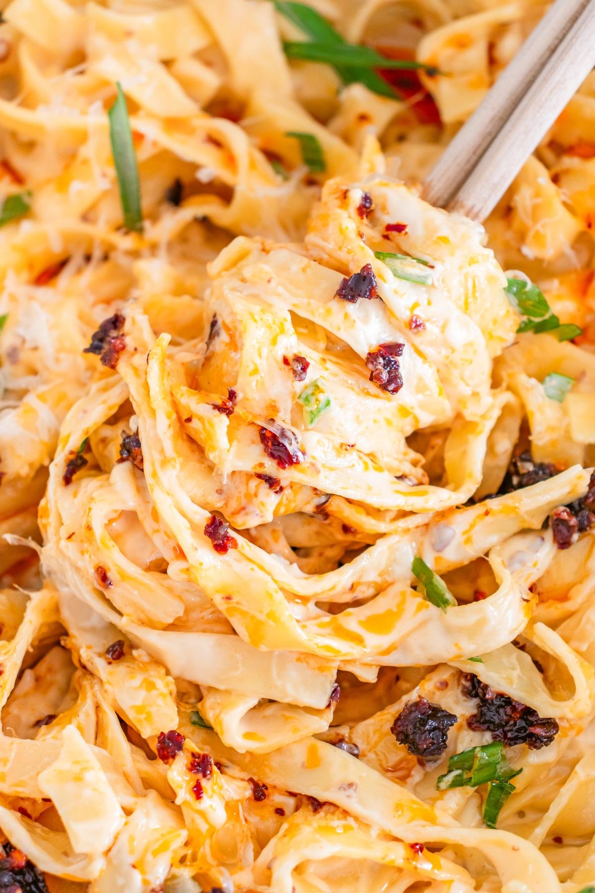 Close-up of creamy noodles with chili flakes and herbs, lifted by chopsticks.