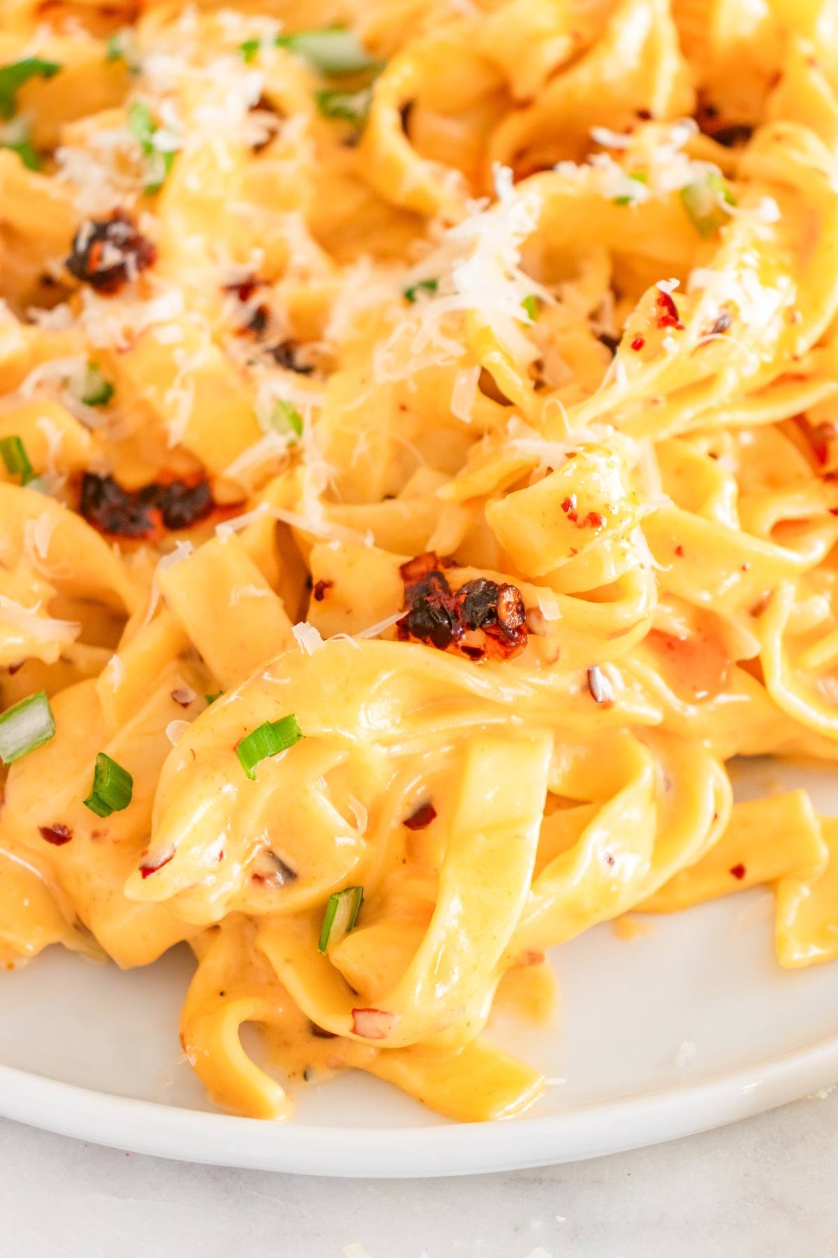 Creamy fettuccine pasta topped with grated cheese, green onions, and red pepper flakes on a white plate.