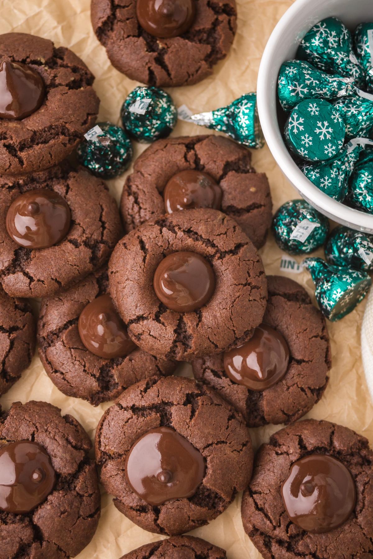 Chocolate mint kiss cookies with melted chocolate centers, surrounded by wrapped chocolate candies in a bowl.
