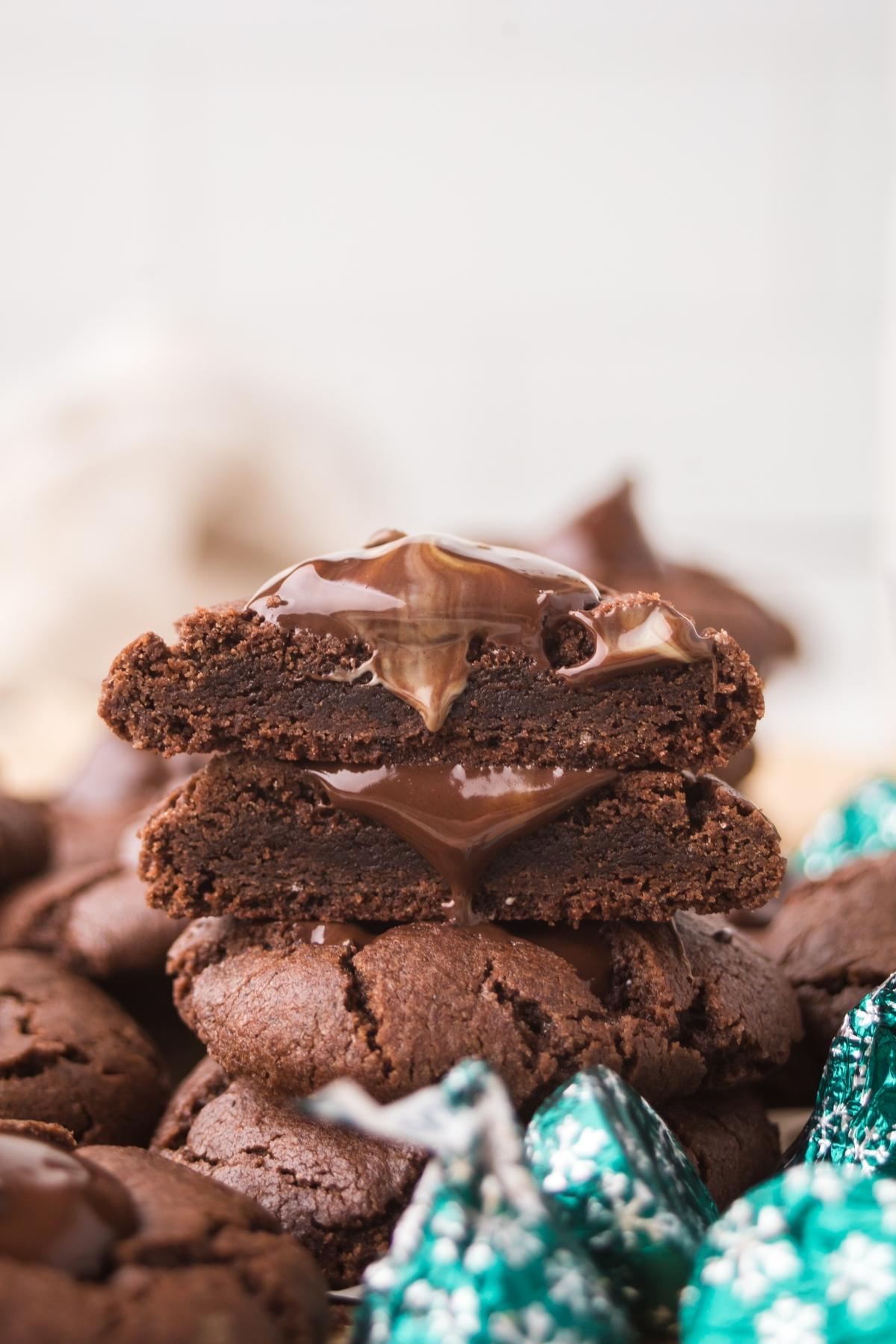 Stacked chocolate mint kiss cookies with gooey melted chocolate in the center, surrounded by wrapped chocolate candies.