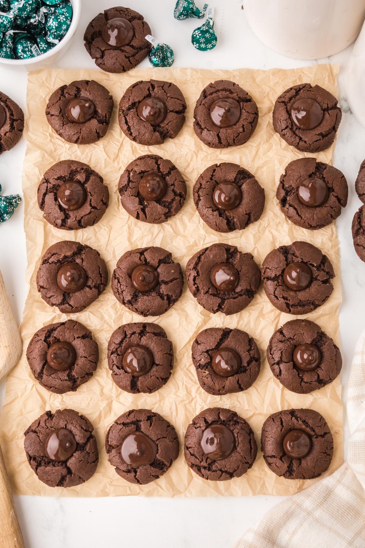 Twenty chocolate mint kiss cookies with chocolate centers arranged on parchment paper, surrounded by baking items.
