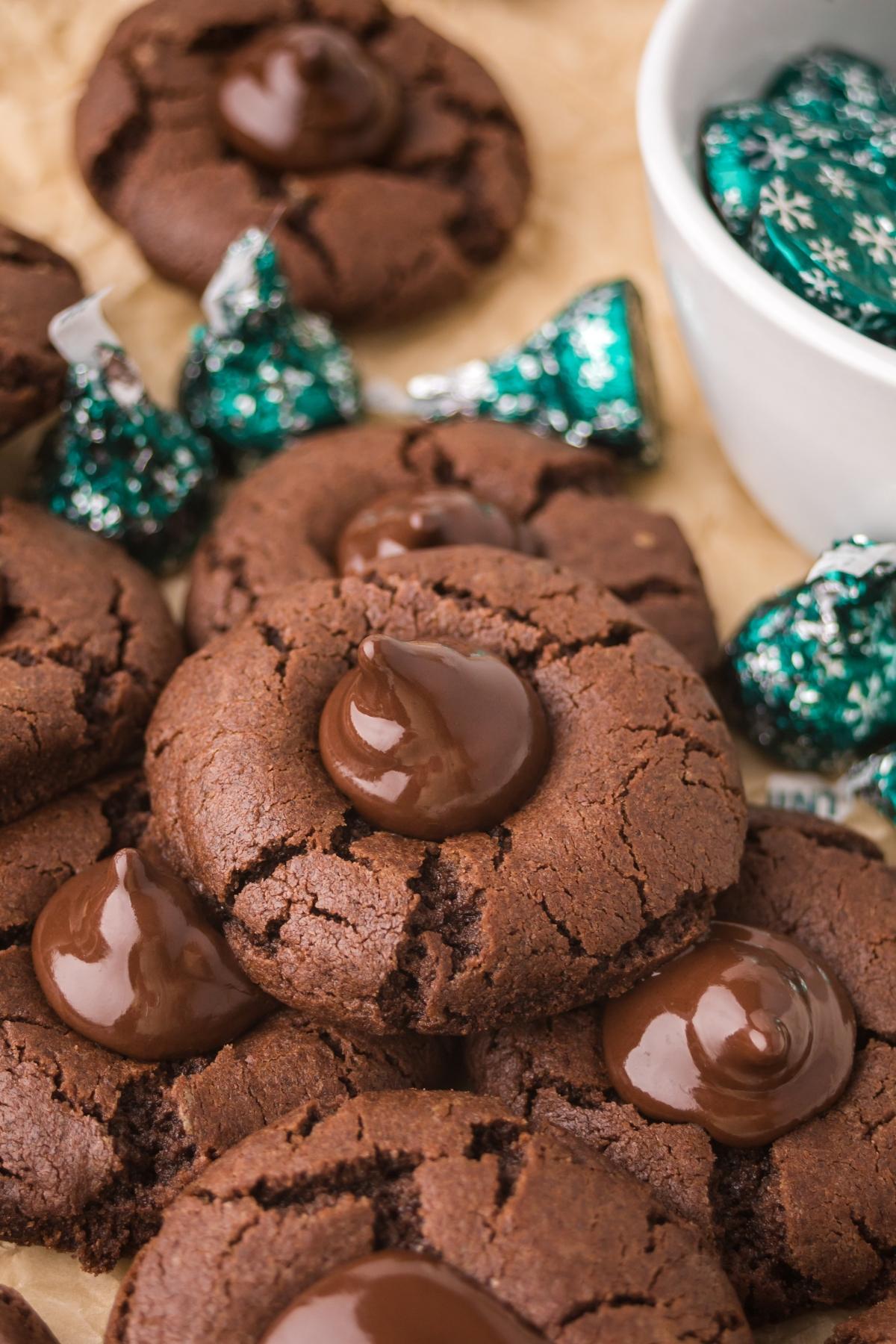 Chocolate mint kiss cookies topped with melted chocolate, surrounded by foil-wrapped chocolate candies.