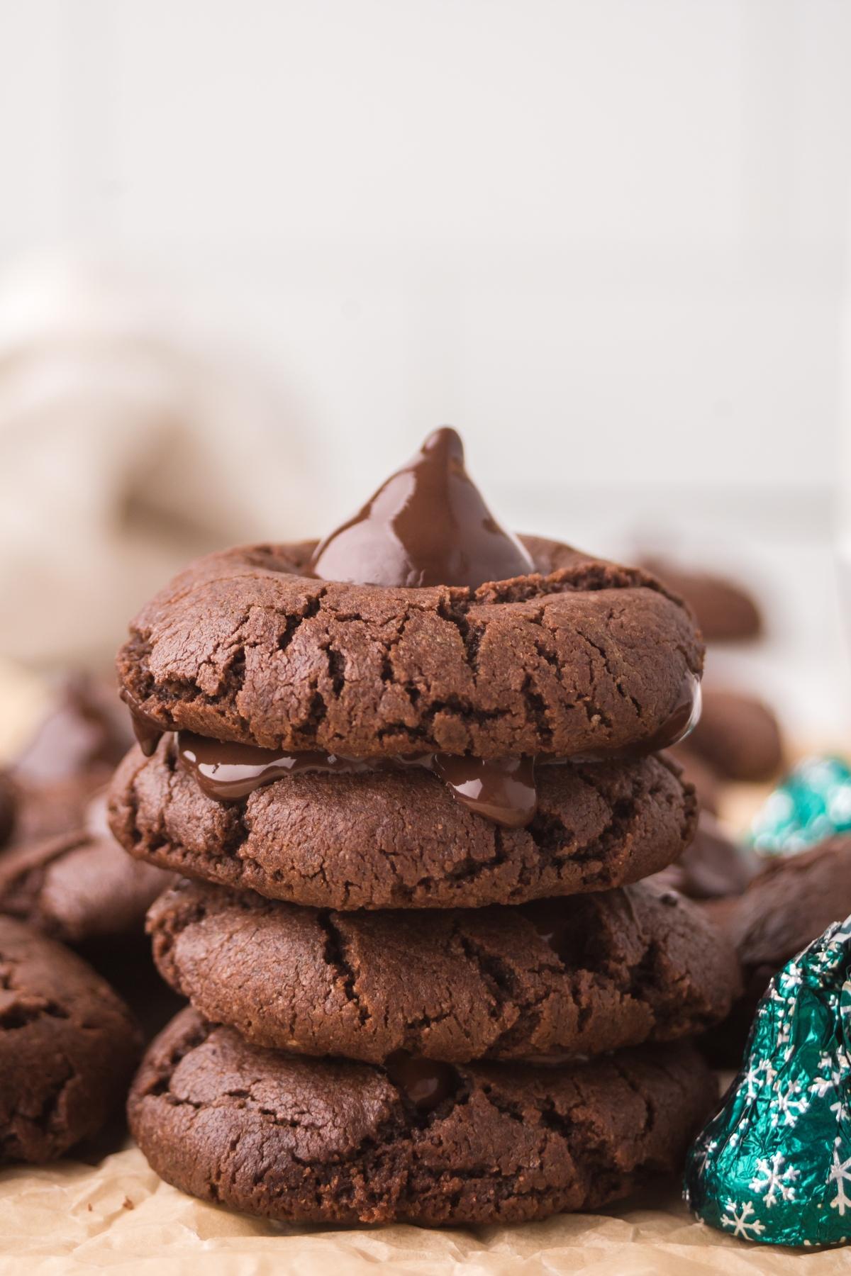 A stack of four chocolate mint kiss cookies with melted chocolate in the center, on parchment paper.