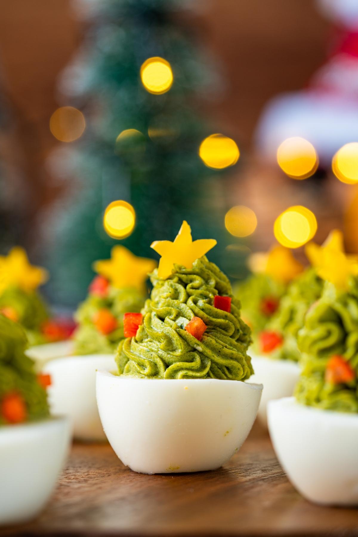 Deviled eggs decorated as Christmas trees with green filling, red bits, and yellow stars on top.