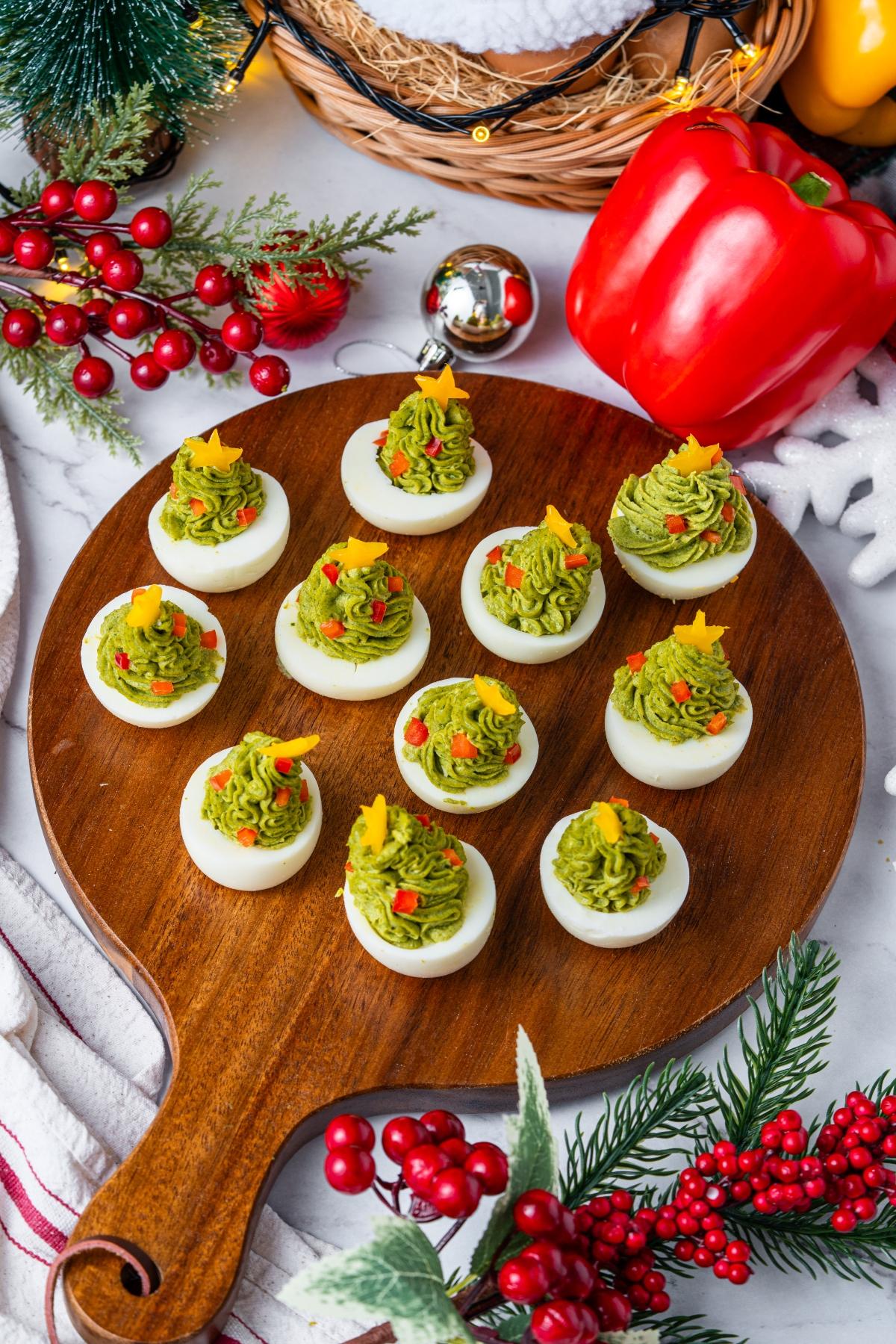 Deviled eggs decorated as Christmas trees with green filling and yellow star toppers on a wooden serving board.