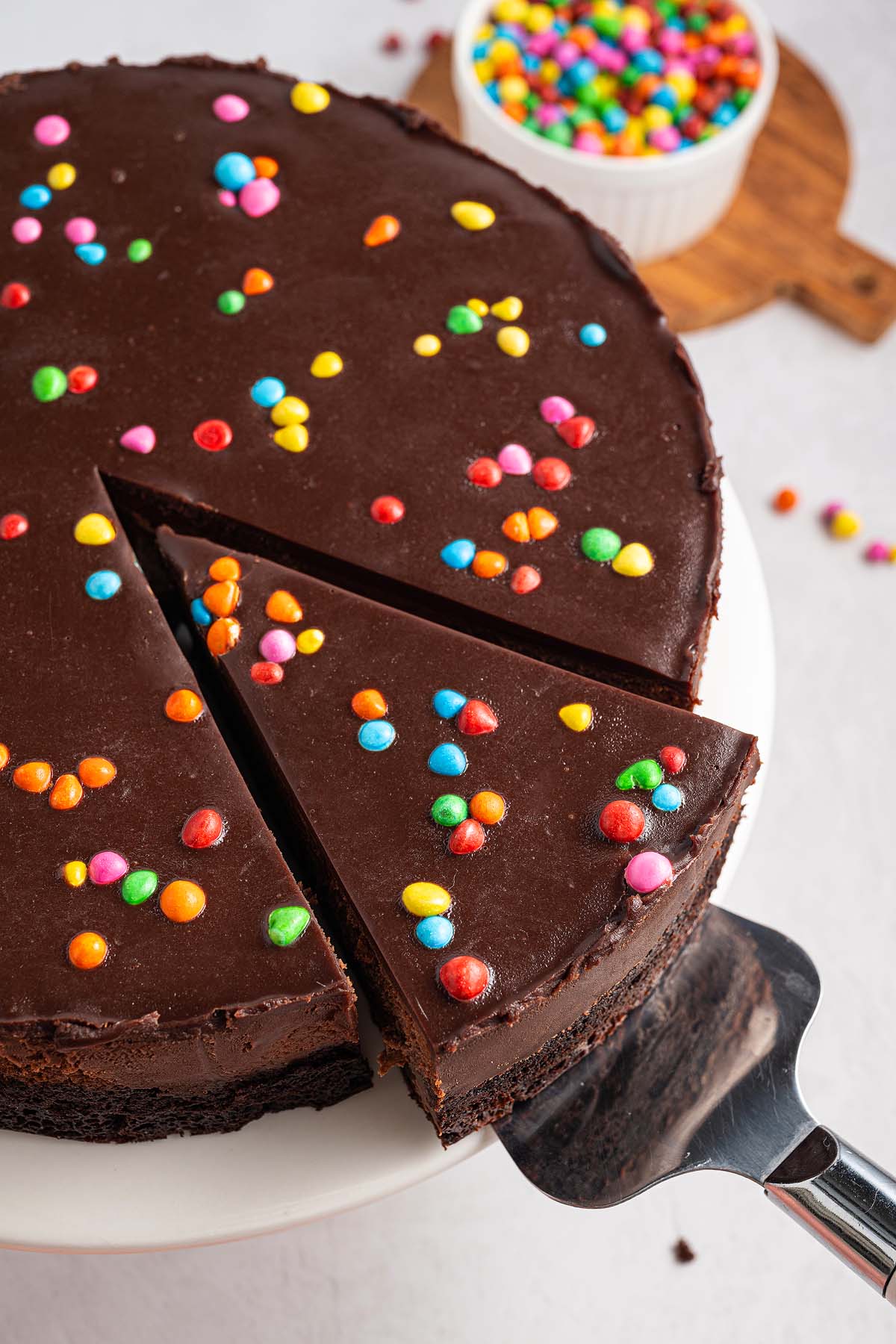 Chocolate cake with colorful candy sprinkles, inspired by Cosmic Brownie Cheesecake, one slice being served on a cake server.