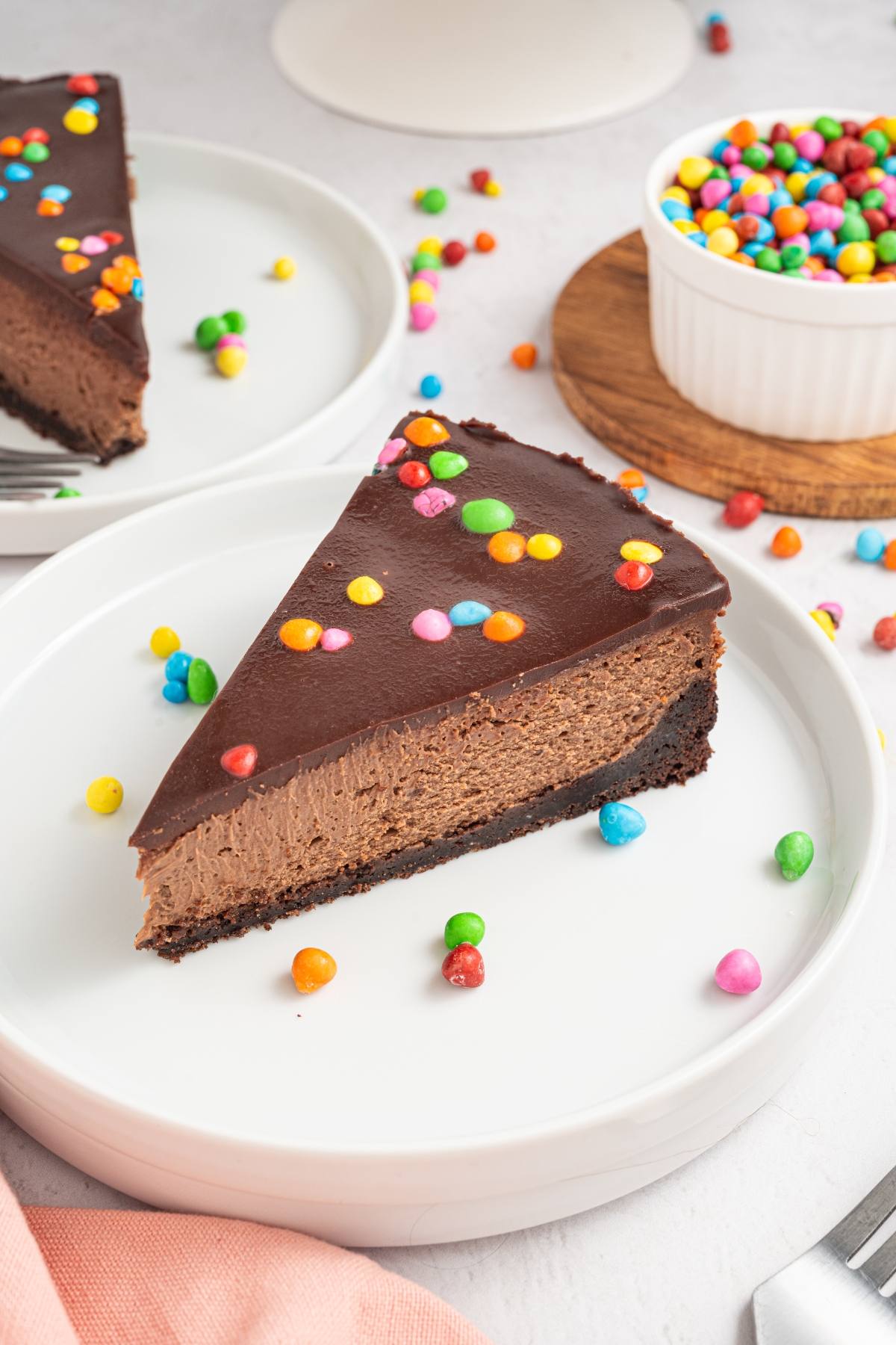 A slice of cosmic brownie cheesecake topped with colorful candy dots on a white plate.