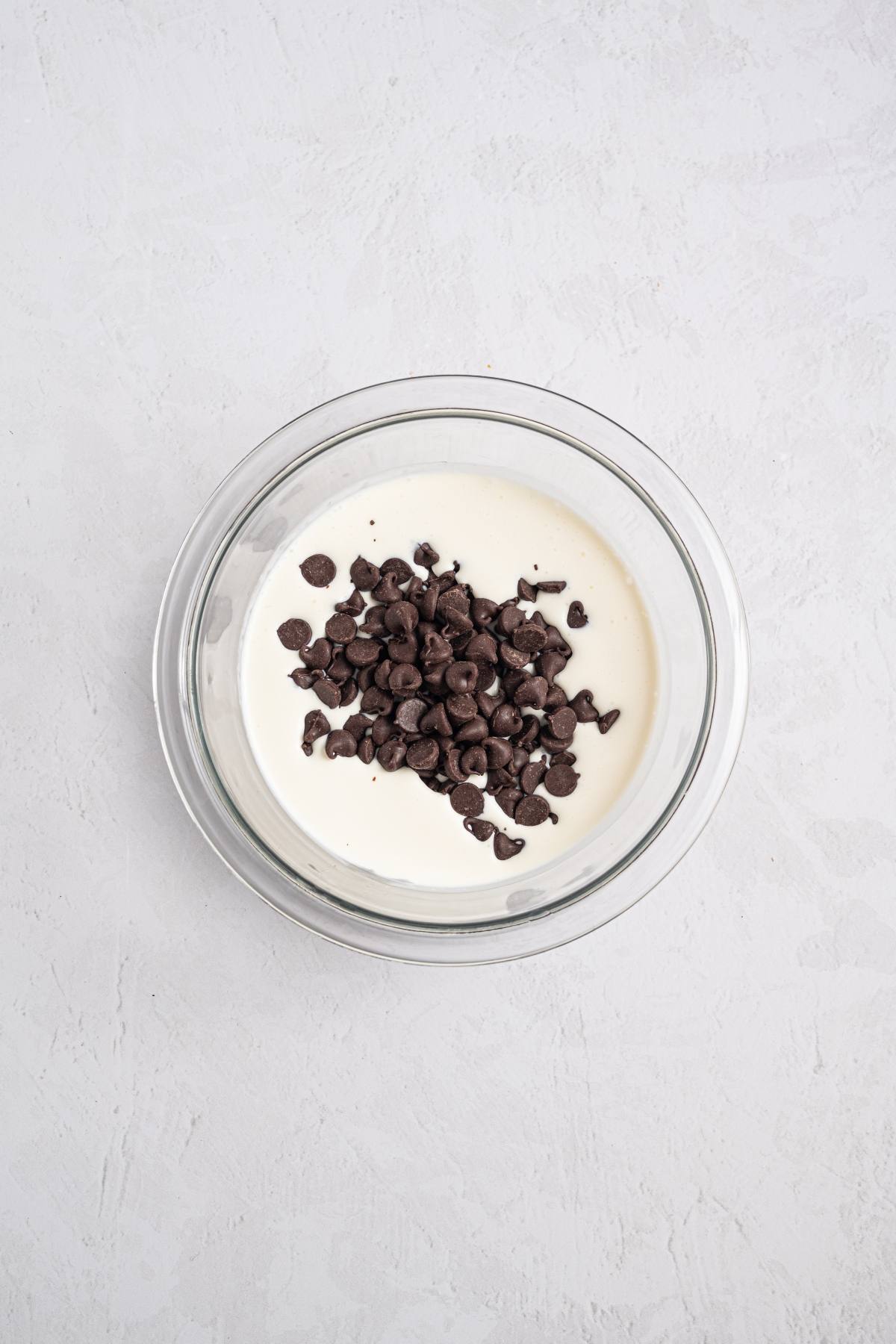 A glass bowl with cream and chocolate chips on a light textured surface.