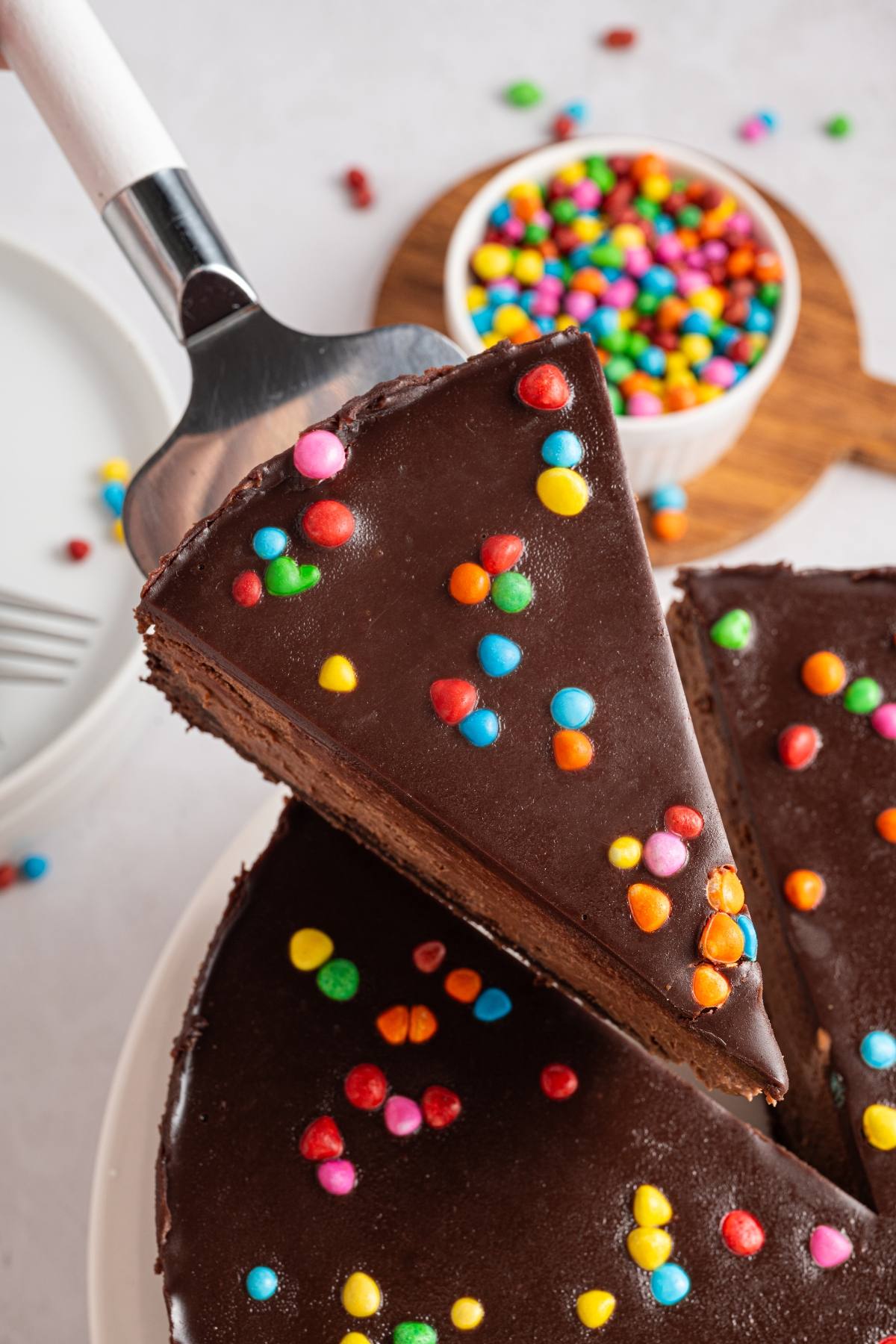 A slice of cosmic brownie cheesecake with colorful candy sprinkles being lifted from the whole cake.