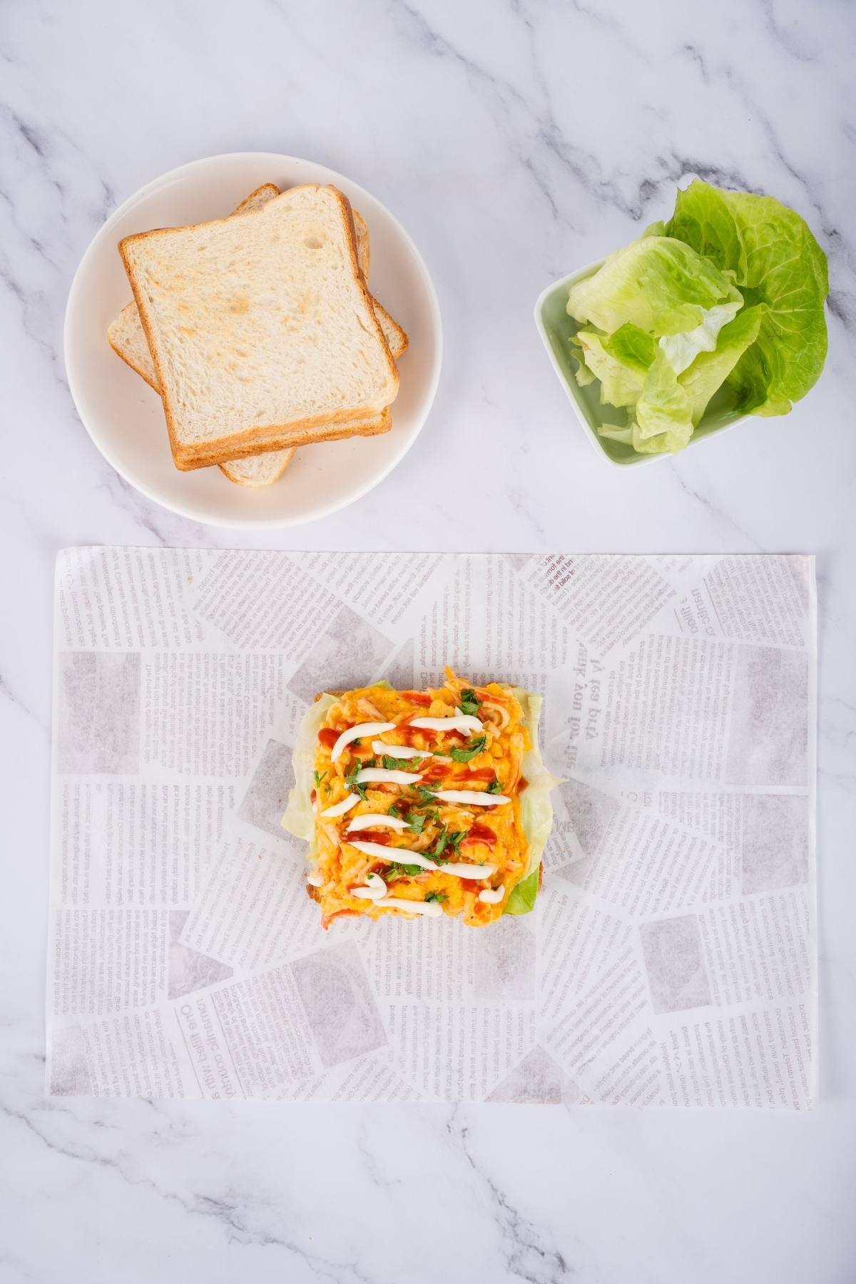 Sandwich ingredients: sliced bread on a plate, lettuce, and a prepared open-faced sandwich on parchment paper.