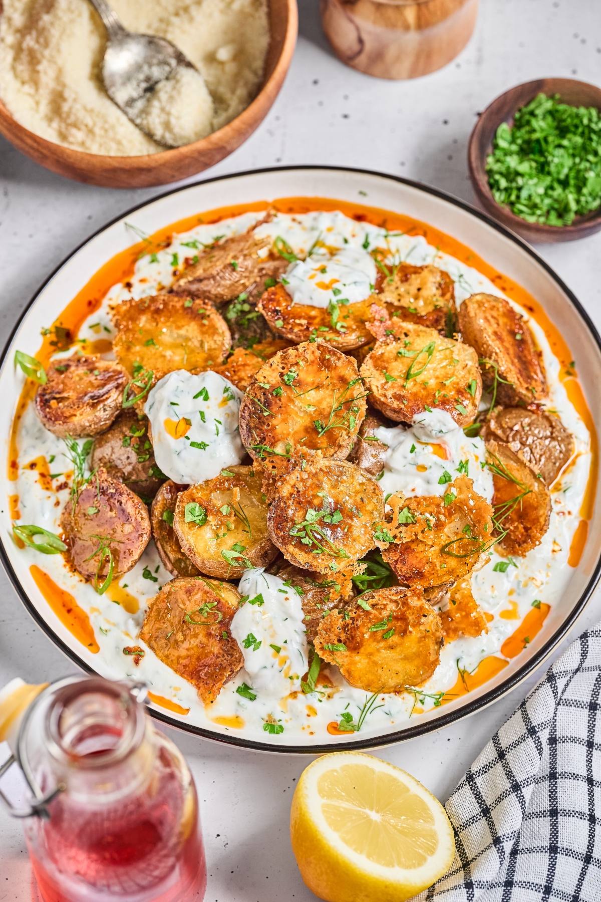 A plate of crispy roasted potatoes topped with creamy sauce and herbs, surrounded by fresh ingredients.