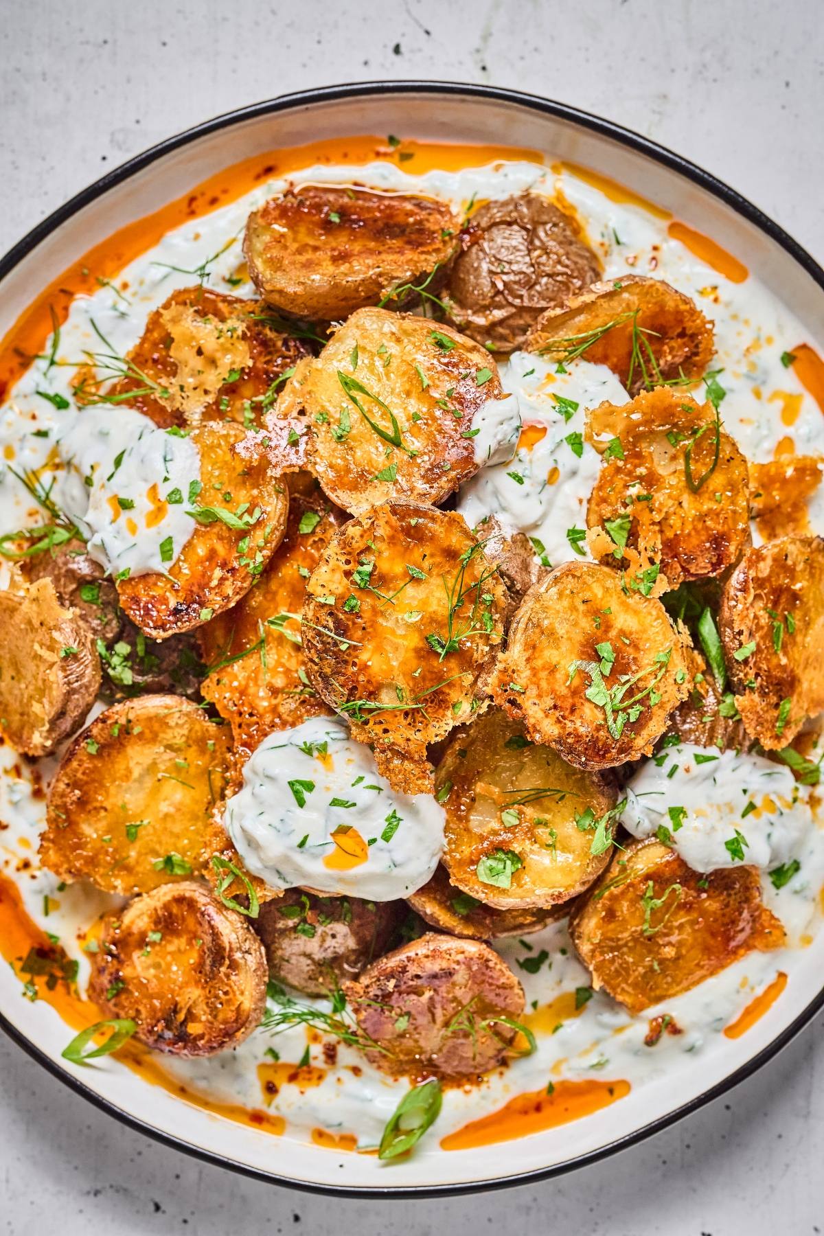 Roasted potatoes topped with creamy white sauce, chopped herbs, and a drizzle of orange oil on a plate.