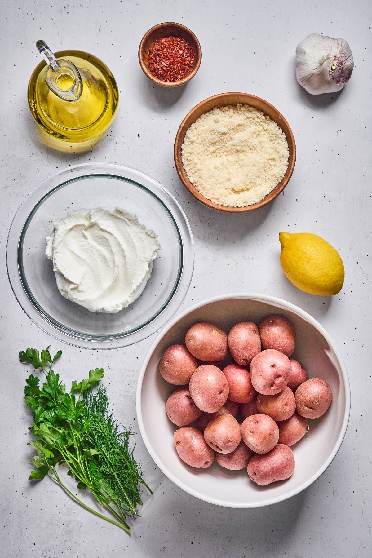 Ingredients on a table: red potatoes, ricotta, parmesan, oil, lemon, garlic, herbs, and chili flakes.