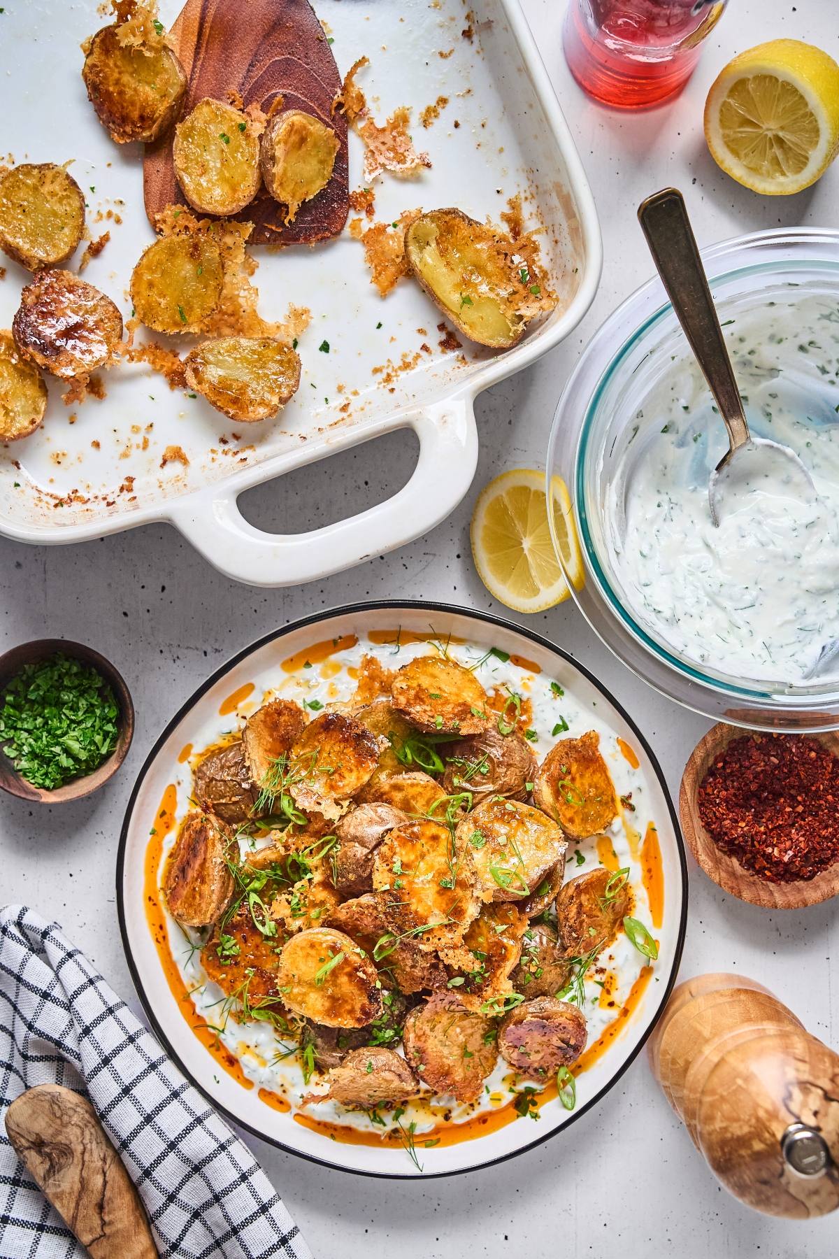 A plate of crispy roasted potatoes with herbs and sauce, surrounded by ingredients and a baking dish.