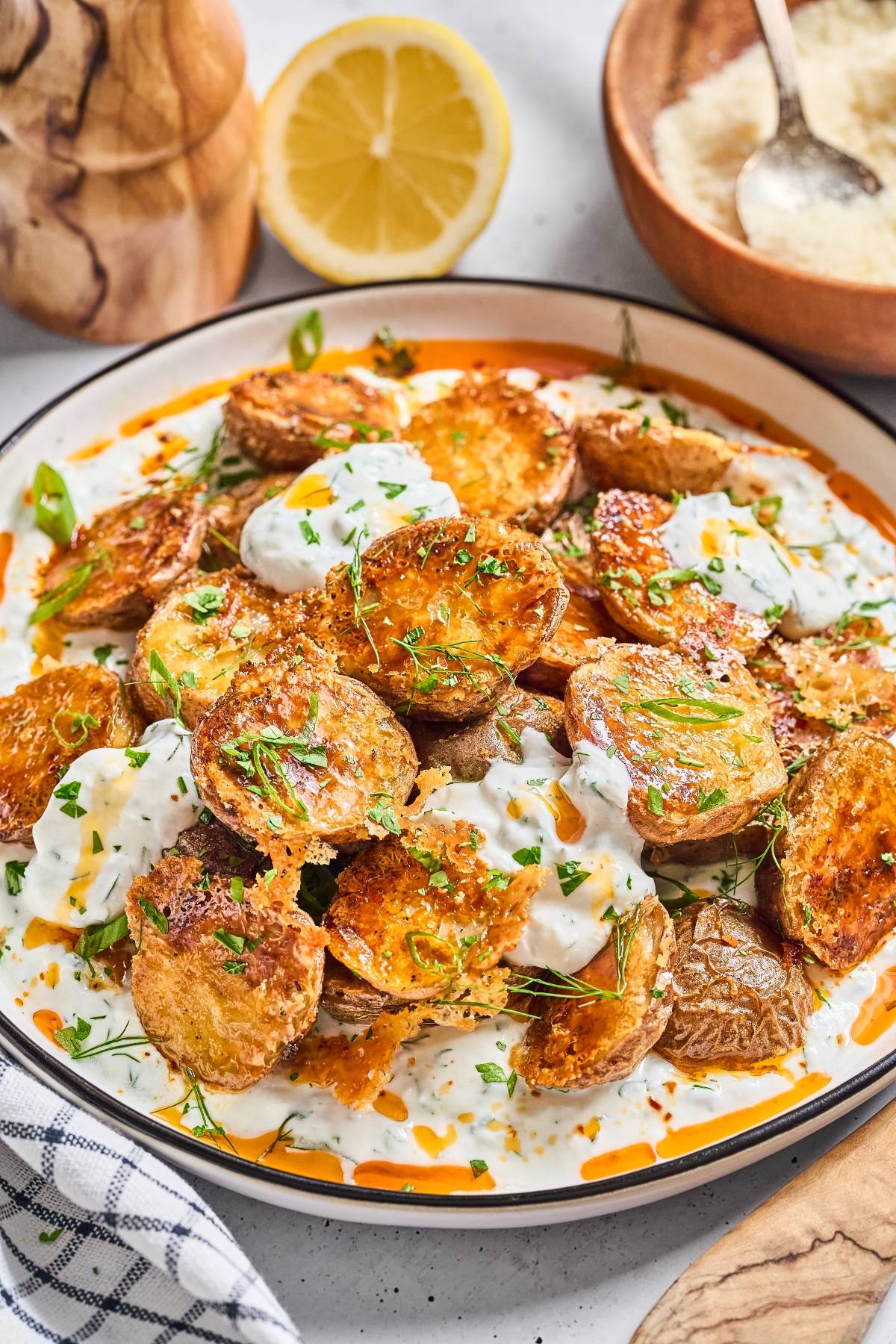 Crispy roasted potato slices on creamy sauce, topped with herbs and a drizzle of oil, served with lemon.