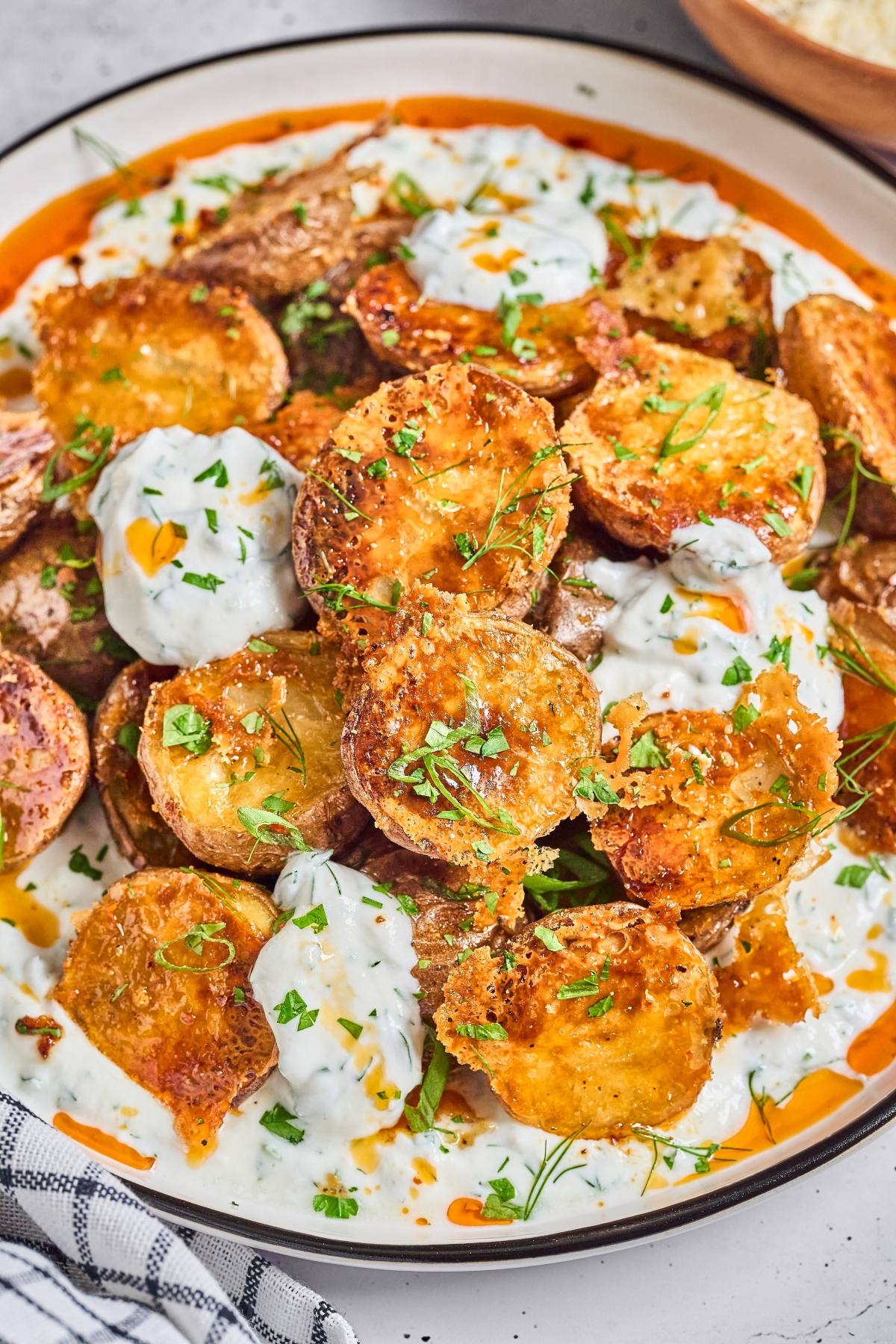 Crispy roasted potatoes topped with creamy sauce, fresh herbs, and a drizzle of oil on a white plate.