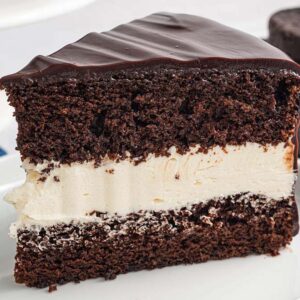 A slice of Ding Dong Cake with creamy white filling and glossy chocolate icing on a white plate.