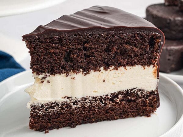 A slice of Ding Dong Cake with creamy white filling and glossy chocolate icing on a white plate.