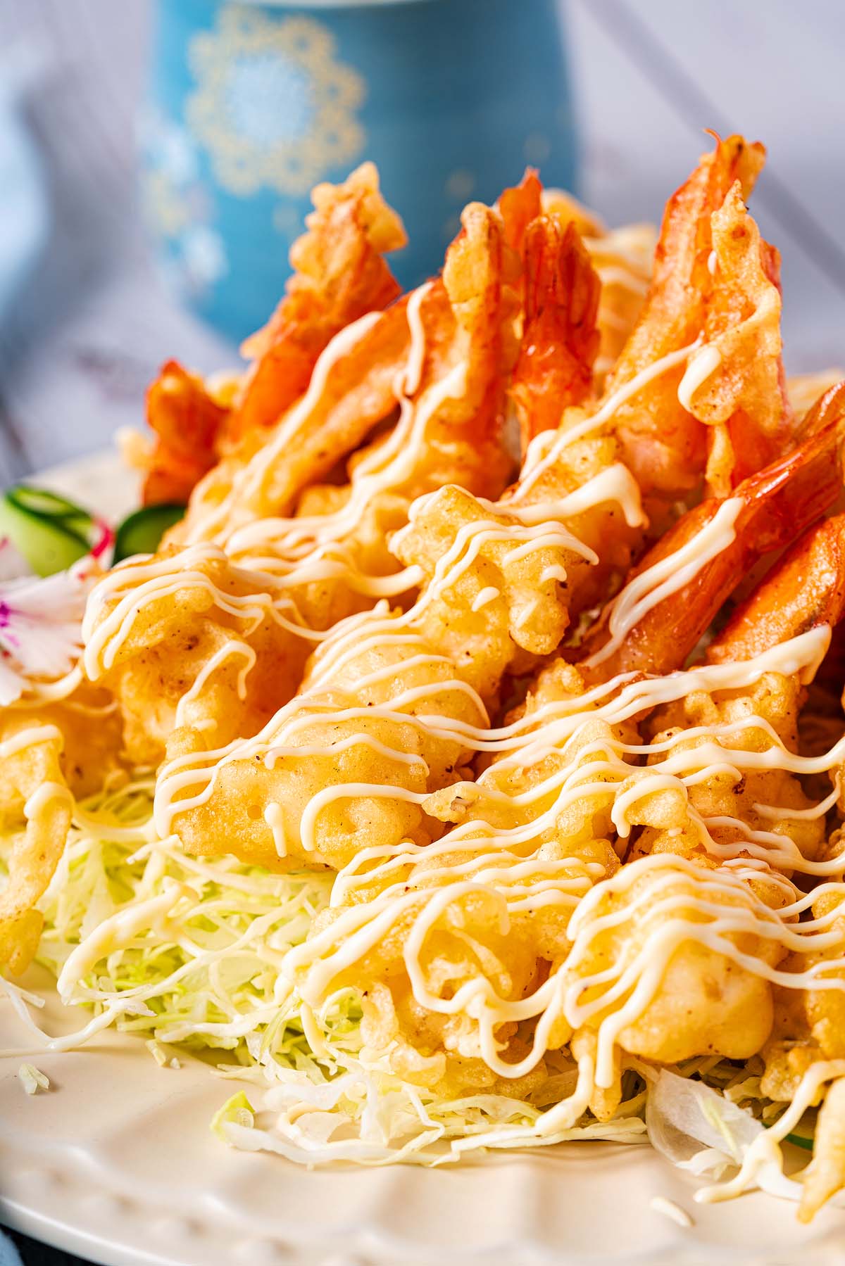 Golden shrimp tempura on shredded cabbage, drizzled with creamy sauce, served on a white plate.