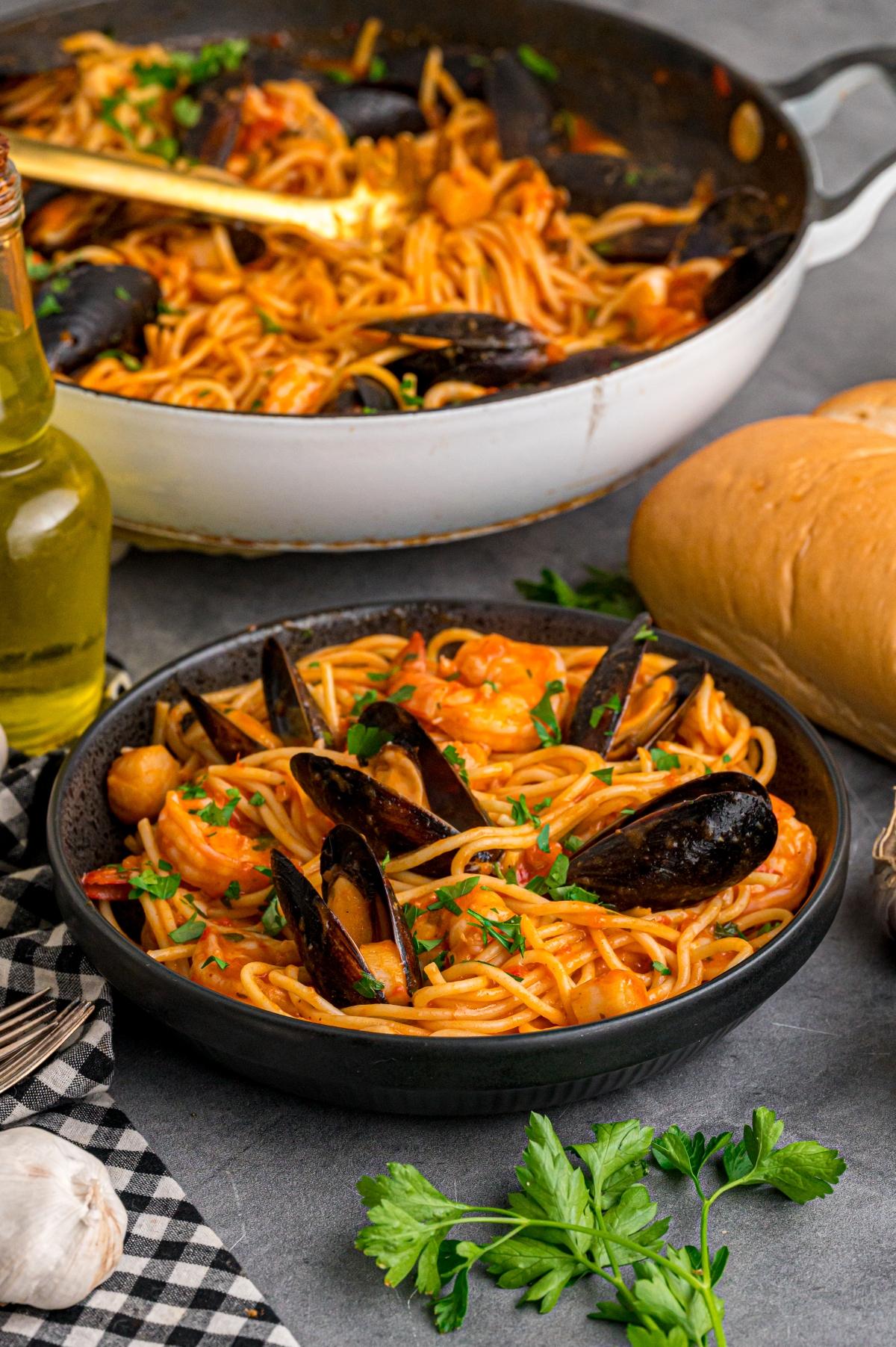 A bowl of seafood pasta with mussels and shrimp, with bread, olive oil, and herbs on the side.