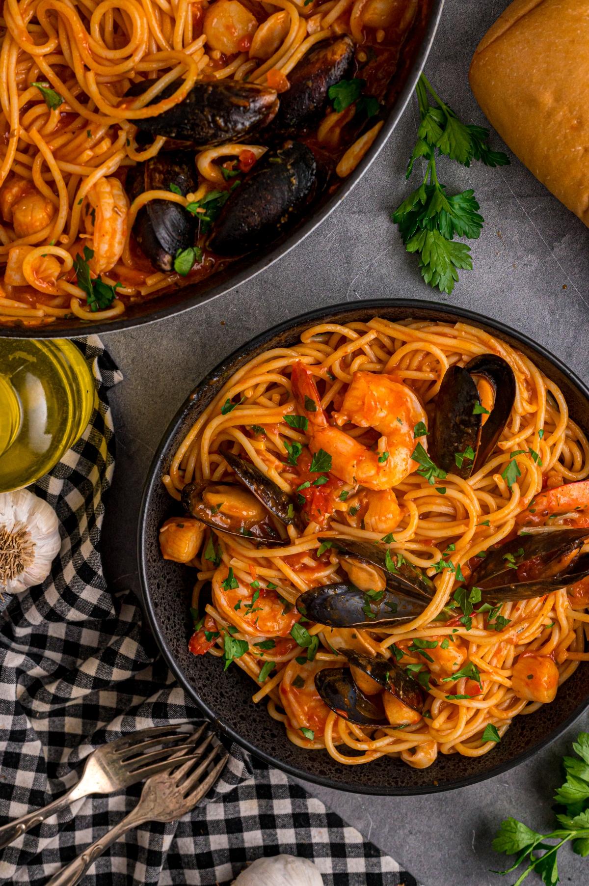 A bowl of seafood spaghetti with shrimp and mussels, garnished with parsley, next to bread and olive oil.