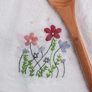 DIY embroidered flour sack towels next to a wooden spoon on a wooden surface.