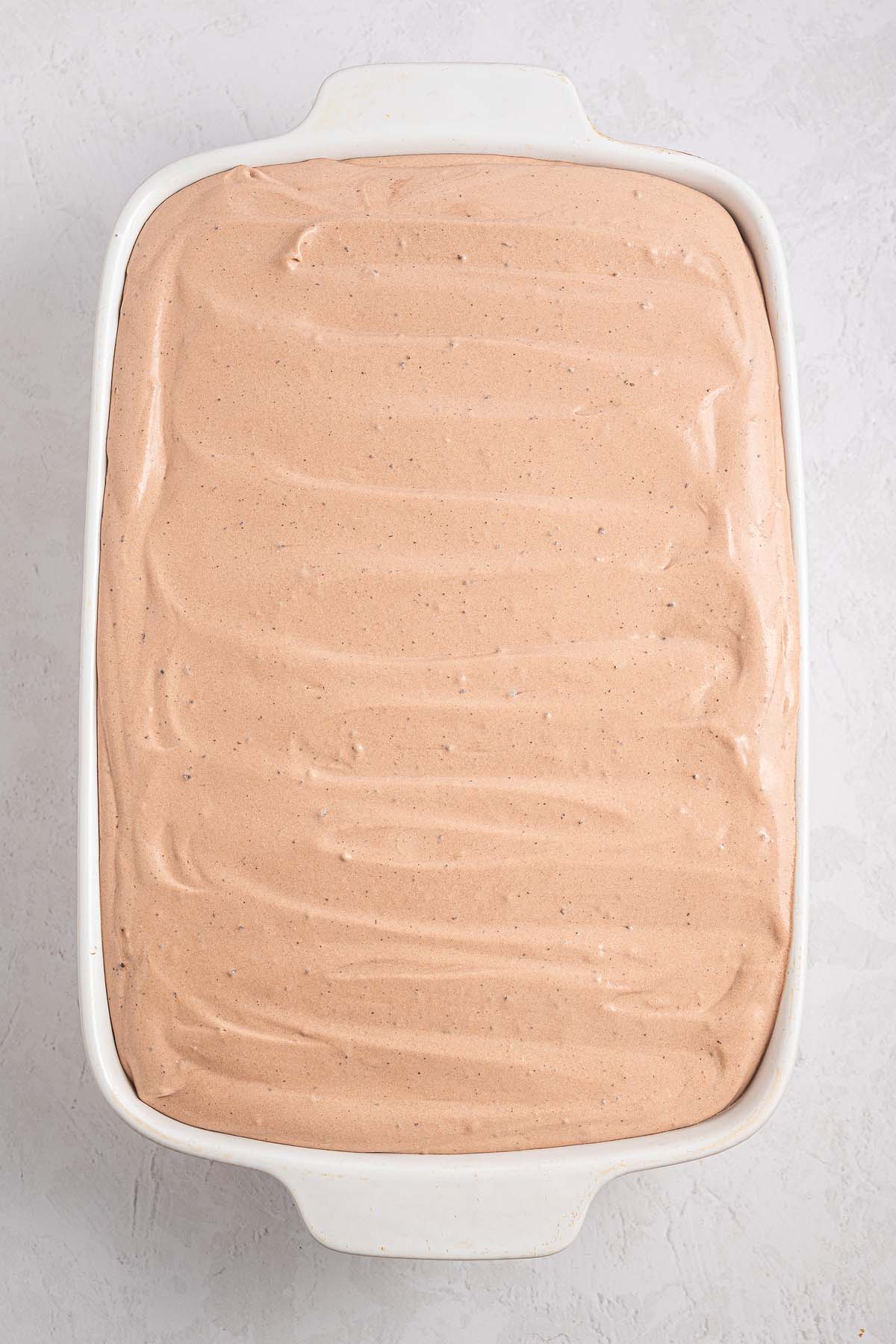A white baking dish filled with smooth, light brown Italian Love Cake mixture sits on a light surface.