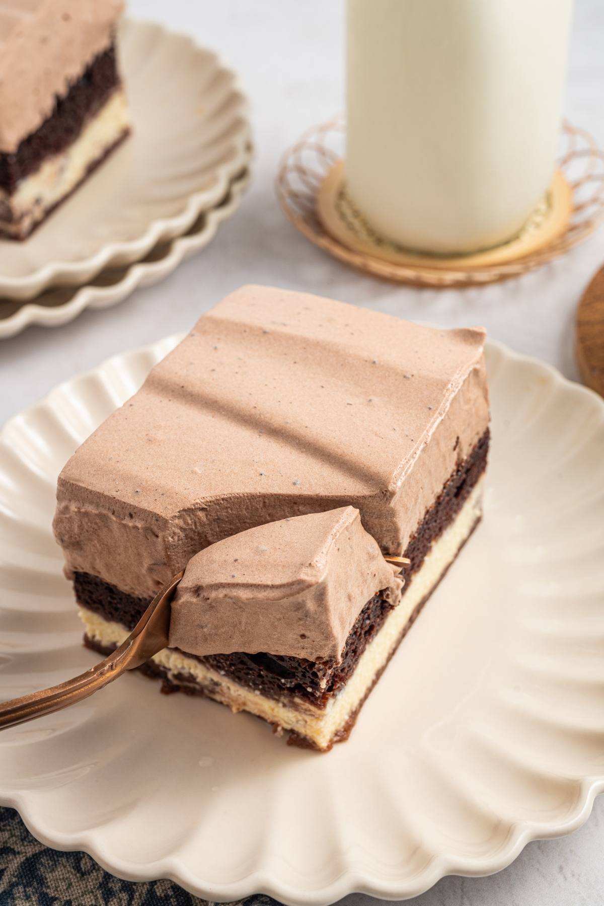 A fork cuts into a layered chocolate dessert with whipped frosting on a white plate.