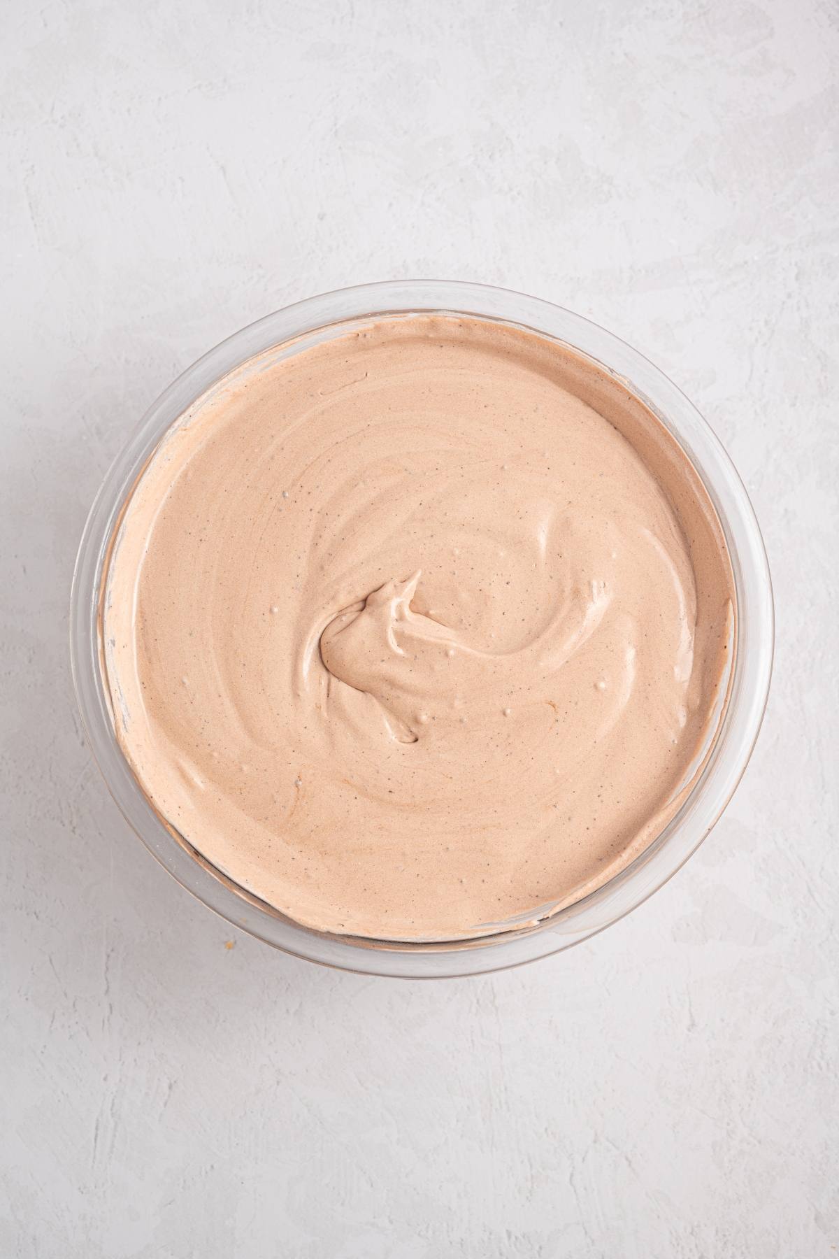 A glass bowl filled with smooth, light brown whipped mixture on a white surface.