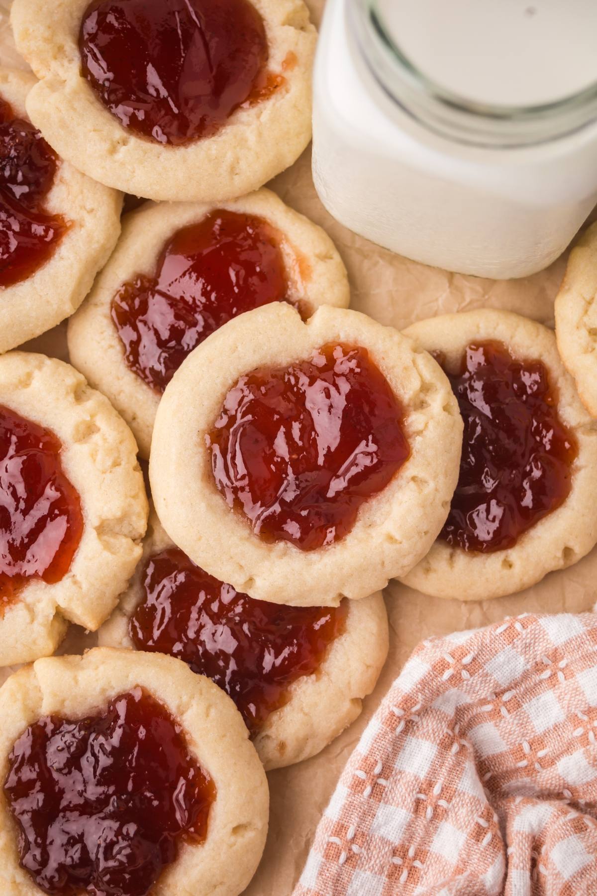 Jam-filled thumbprint cookies next to a bottle of milk and a checked cloth.