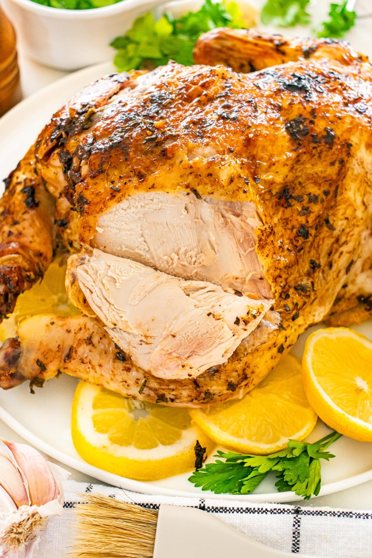 Roast chicken on a plate with sliced breast, garnished with lemon wedges and fresh parsley.