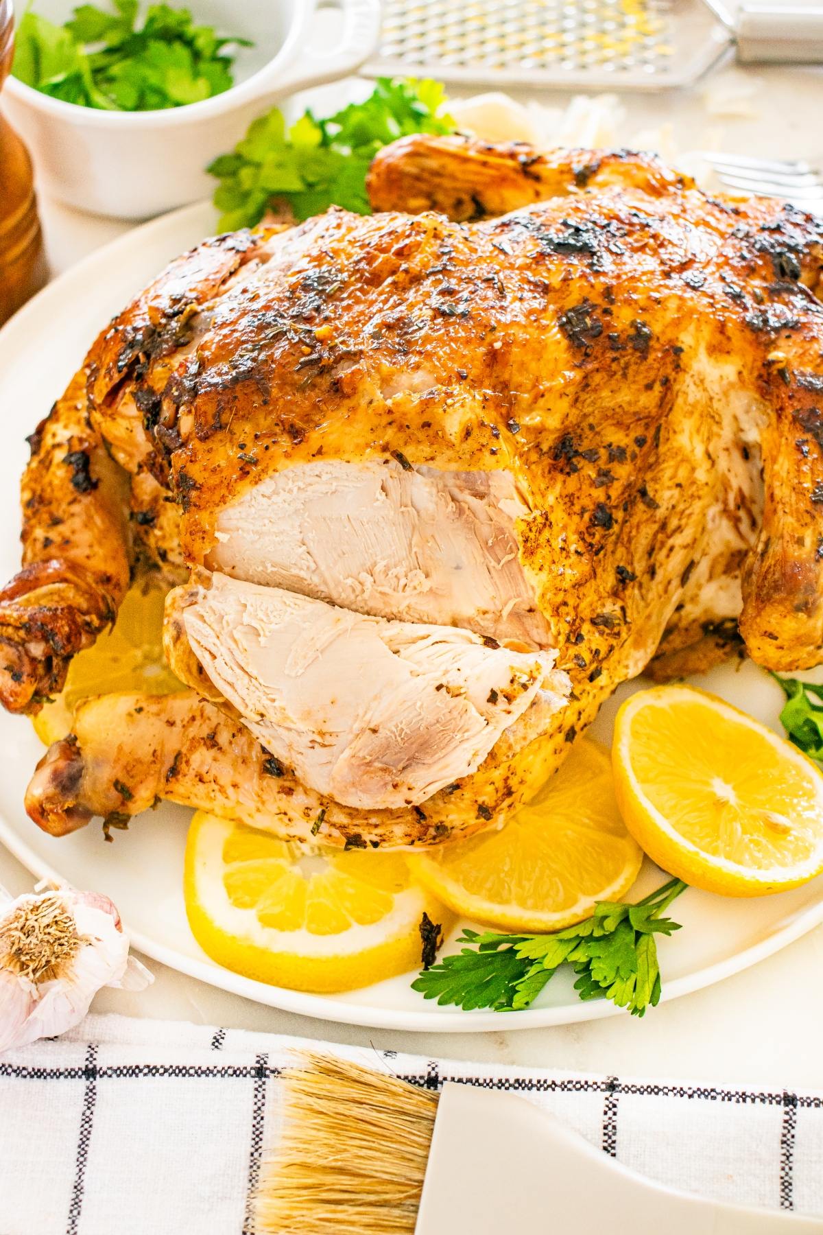 Roast chicken with sliced breast, garnished with lemon slices and parsley on a white plate.
