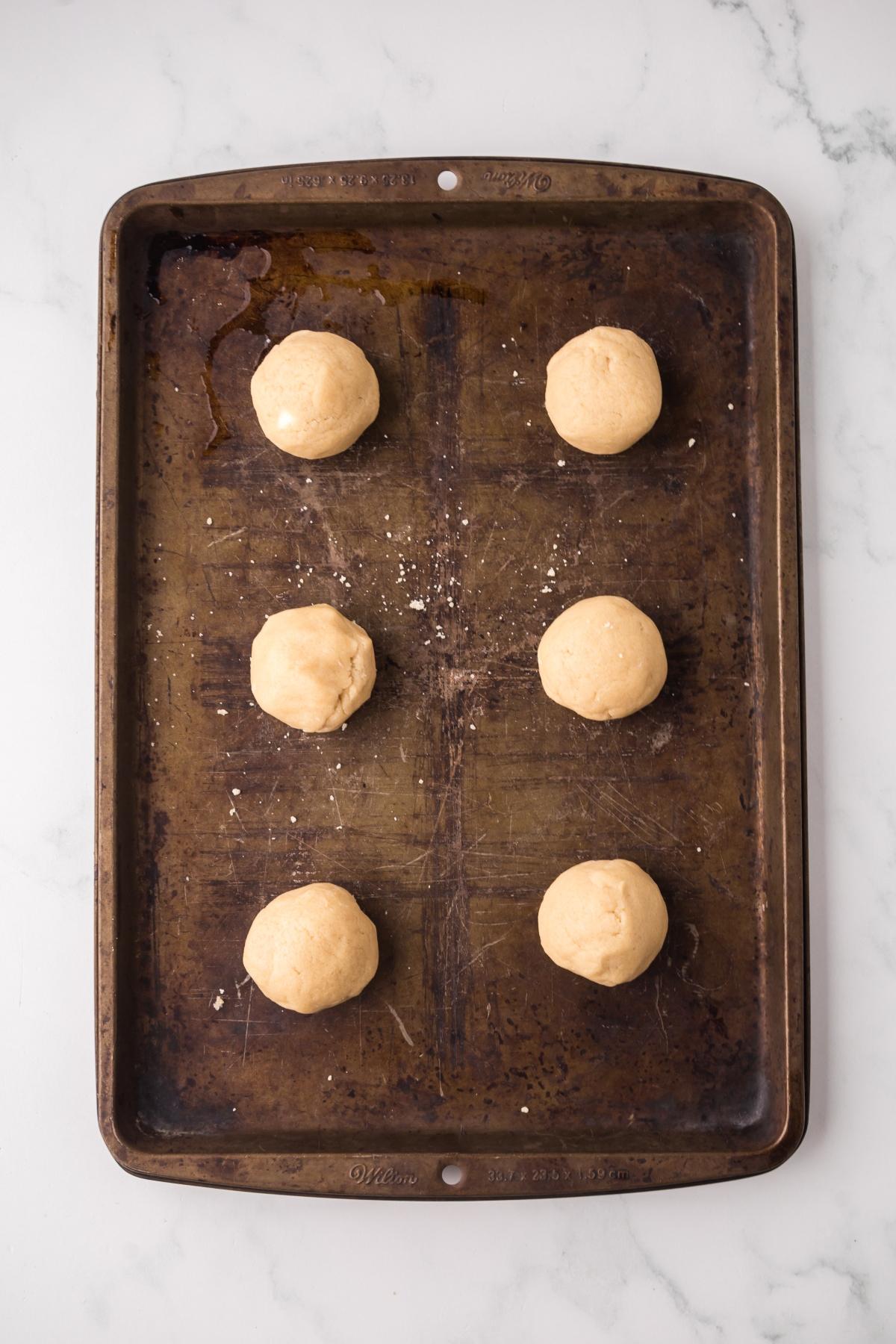 Six balls of cookie dough arranged in two columns on a baking sheet, ready to be baked.