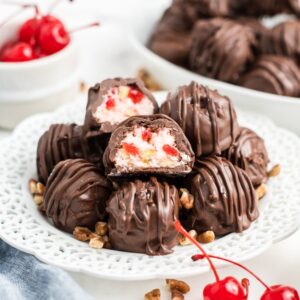 Chocolate-covered Martha Washington Candy sits on a white plate, surrounded by chopped nuts and fresh cherries for a classic sweet treat.