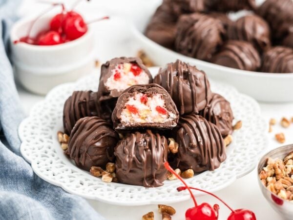 Chocolate-covered Martha Washington Candy sits on a white plate, surrounded by chopped nuts and fresh cherries for a classic sweet treat.