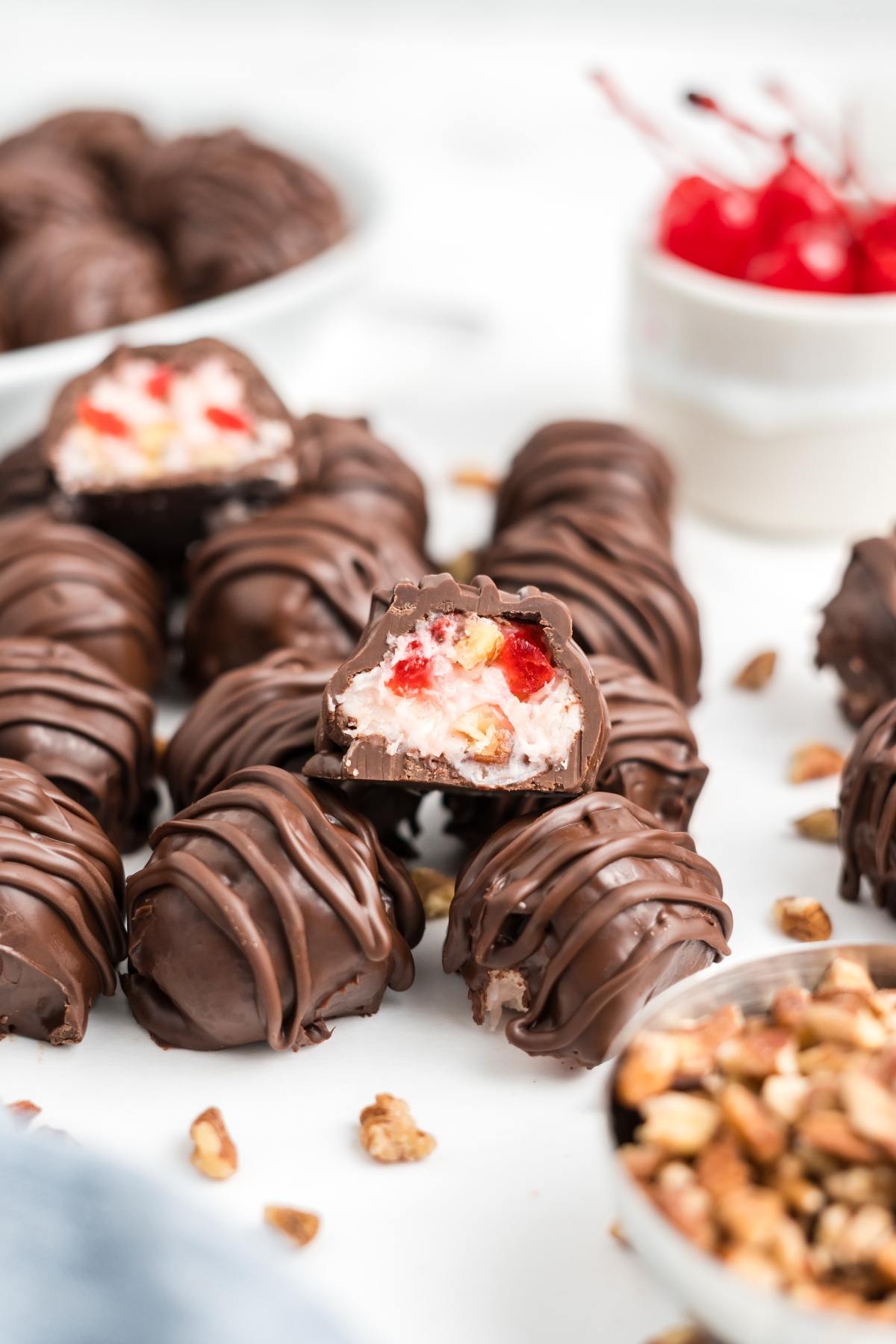 Chocolate-covered martha washington candies with a creamy cherry and nut filling, some whole and some cut open, on a white surface.