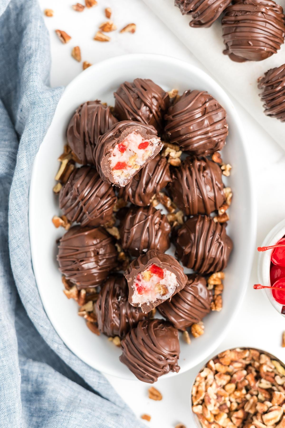 A bowl of chocolate-covered martha washington candies with cherry and coconut filling, some cut open, on chopped pecans.