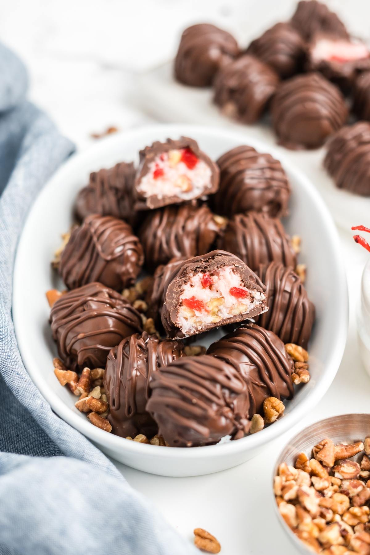 Chocolate-covered martha washington candies with pecans and cherry filling, shown whole and halved in a white dish.