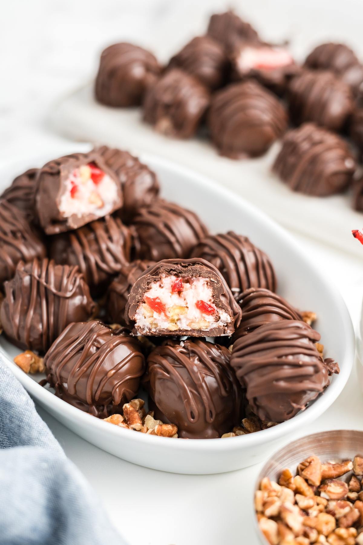A plate of chocolate-covered martha washington candies, some cut open to reveal a cherry and cream filling, with pecans nearby.