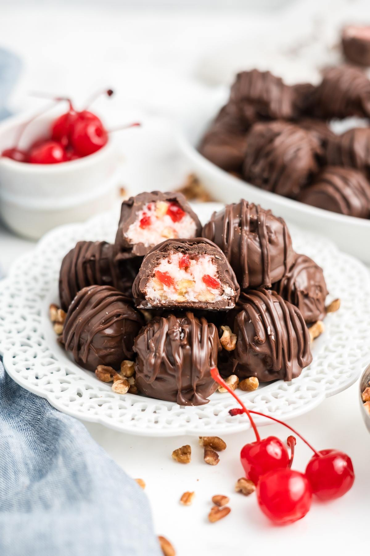 Chocolate-covered cherry martha washington candies stacked on a white plate, with whole cherries and pecans scattered around.