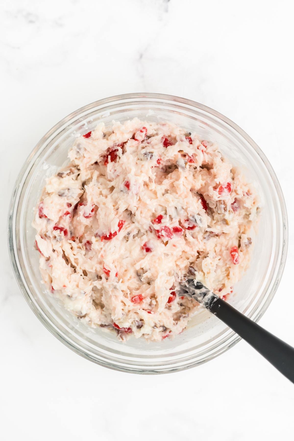 A glass bowl filled with creamy dip mixed with red and brown bits, and a black spoon inside.