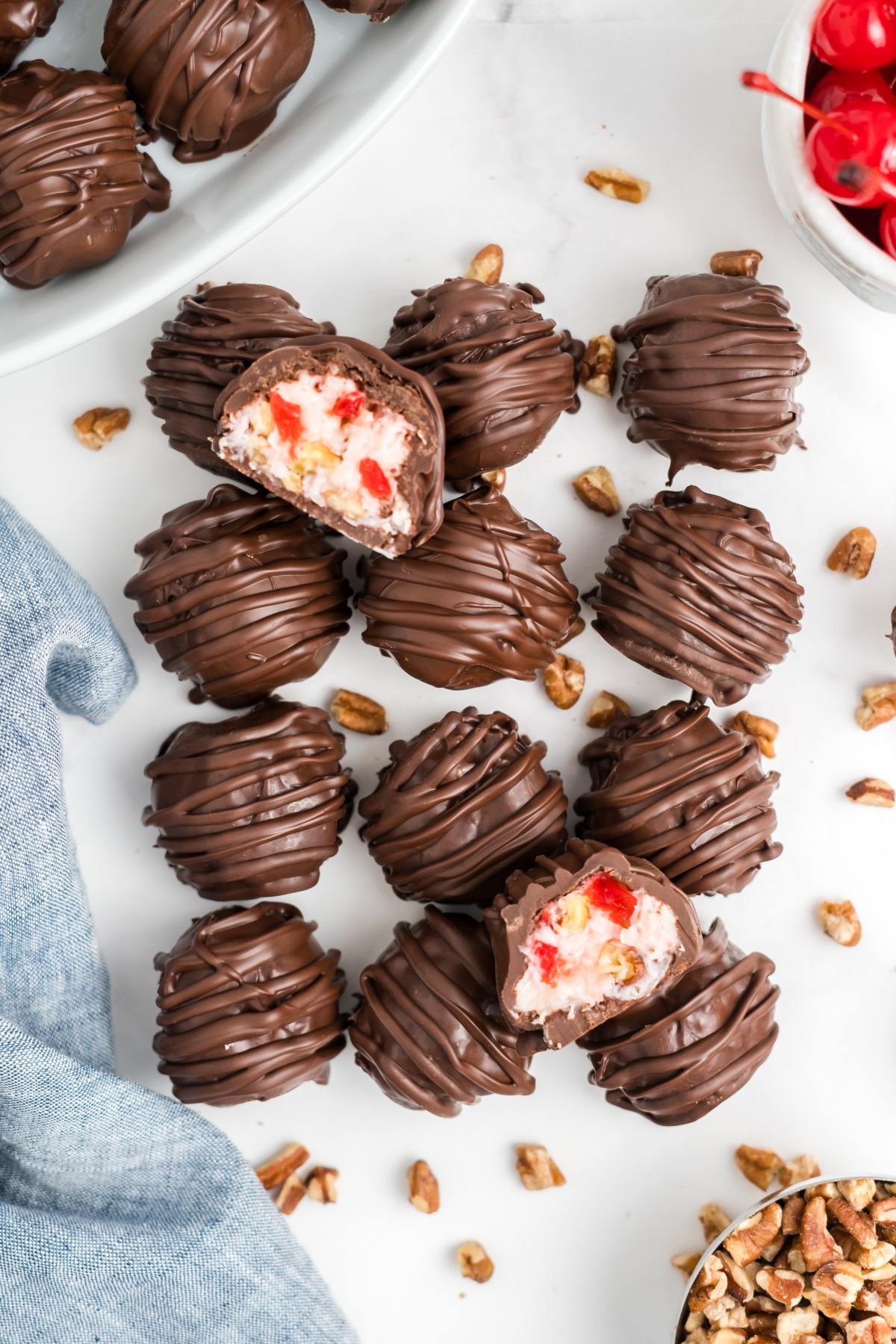 Chocolate-covered cherry and nut martha washington candies, some cut open to show creamy cherry filling, arranged on a white surface.
