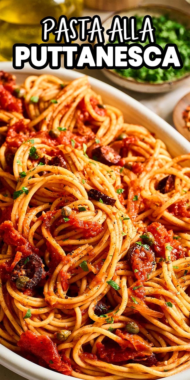 A close-up of Pasta Puttanesca with tomato sauce, olives, and herbs in a white dish.