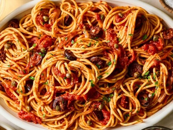Pasta Puttanesca: Spaghetti with tomato sauce, olives, and capers served in a white oval dish, garnished with fresh herbs.
