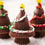 Three Peanut Butter Cup Christmas Trees made from stacked chocolate cups, decorated with icing, sprinkles, and star toppers.