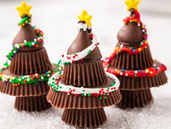 Three Peanut Butter Cup Christmas Trees made from stacked chocolate cups, decorated with icing, sprinkles, and star toppers.